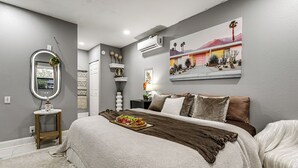 A bedroom with a bed, a bedside table, a wall-mounted air conditioner, a framed picture, and a mirror. - Group-Ready Oasis w/ Pool & Games in Port Richey (Port Richey)