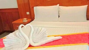 A hotel room with a bed, pillows, a nightstand, and a decorative towel arrangement.