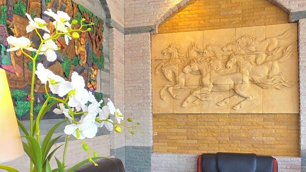 A lobby with a sofa, chairs, a small table, a potted plant, and a decorative wall with a relief sculpture.