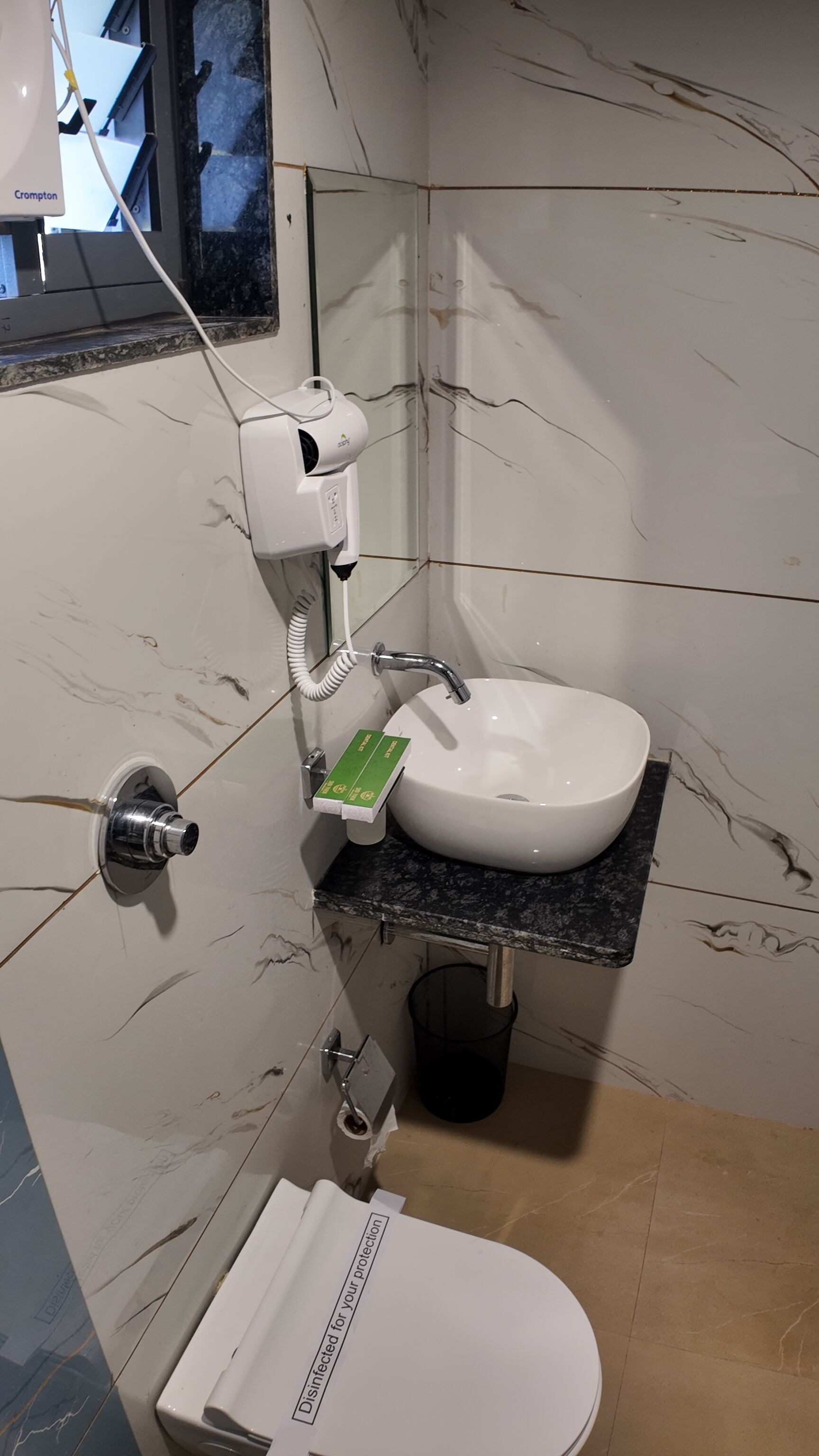 Un baño con lavamanos blanco, inodoro y secador de pelo en la pared.