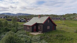 A rural house with a red door and grey roof, surrounded by greenery and other houses.