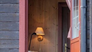 A wooden cabin entrance with a lamp, a table, and a chair.