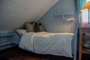 A small, single-bed room with a sloped ceiling, a wooden headboard, and a bedside table with a lamp.