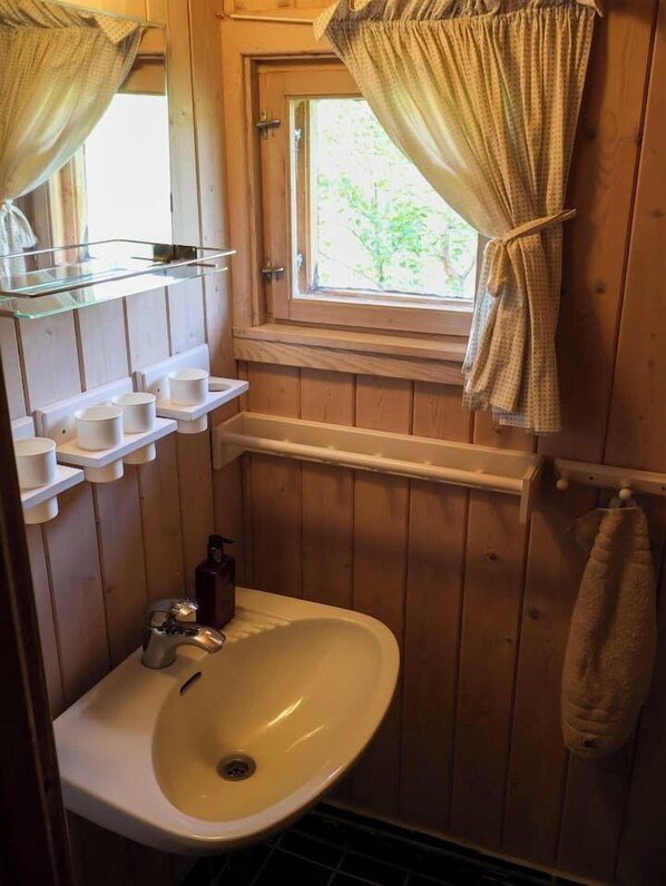 Une salle de bain en bois avec un lavabo, un miroir et une fenêtre avec des rideaux.