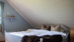 A bedroom with a sloped ceiling, a bed with a white mattress and pillows, a wooden nightstand, and a fur throw on the bed.