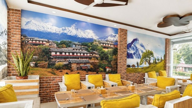 A restaurant with a mountain mural, wooden tables, and yellow cushions.