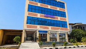 A multi-story building with a blue glass facade, a sign reading 'Authentic Nepal,' and a parking lot in front.