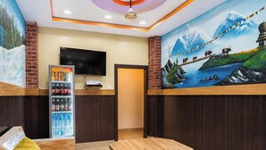 A hotel lobby with a reception desk, a television, a beverage refrigerator, a mural, and seating area.