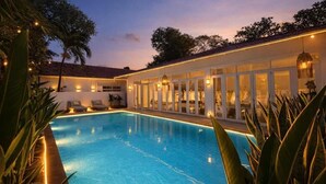 A swimming pool with a glass enclosure, surrounded by plants and a building with large windows. - Gorgeous Grand Pool Villa in D2 by Ray (Ho Chi Minh City)