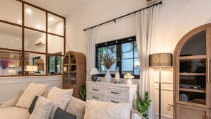 A living room with a sofa, a cabinet, a lamp, and a window with curtains. - Gorgeous Grand Pool Villa in D2 by Ray (Ho Chi Minh City)
