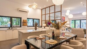 A modern kitchen with a central island, large windows, and a dining area with round tables. - Gorgeous Grand Pool Villa in D2 by Ray (Ho Chi Minh City)