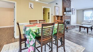 Uma sala de estar com área de jantar, mesa posta para quatro pessoas, cadeiras, lareira e sofá.