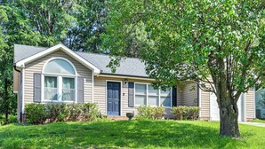 Uma casa térrea com um jardim frontal, uma grande árvore e uma garagem.