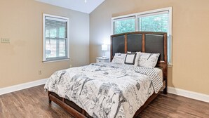 Quarto com cama de madeira, duas mesas de cabeceira, um criado-mudo e uma janela com persianas.