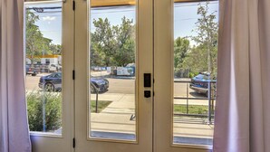 Blick durch eine Tür mit Fenster auf eine Straße mit parkenden Autos und ein Gebäude im Hintergrund.
