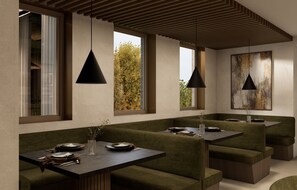 A modern dining area with green upholstered seating, pendant lighting, and large windows offering views of trees. - The Point Slovenia (Gorišnica)