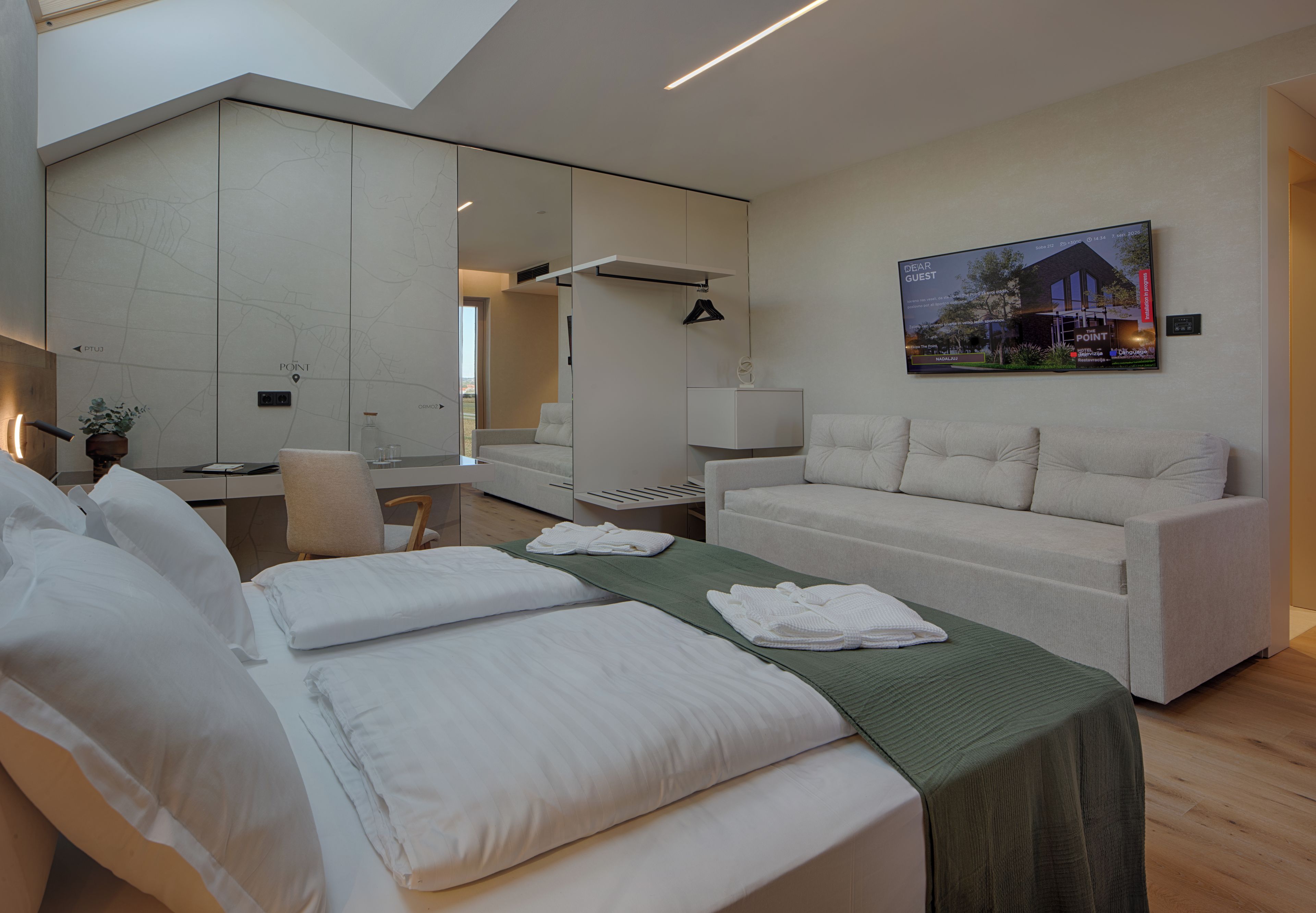 A modern hotel room with a bed, a sofa, a desk, and a large mirror.