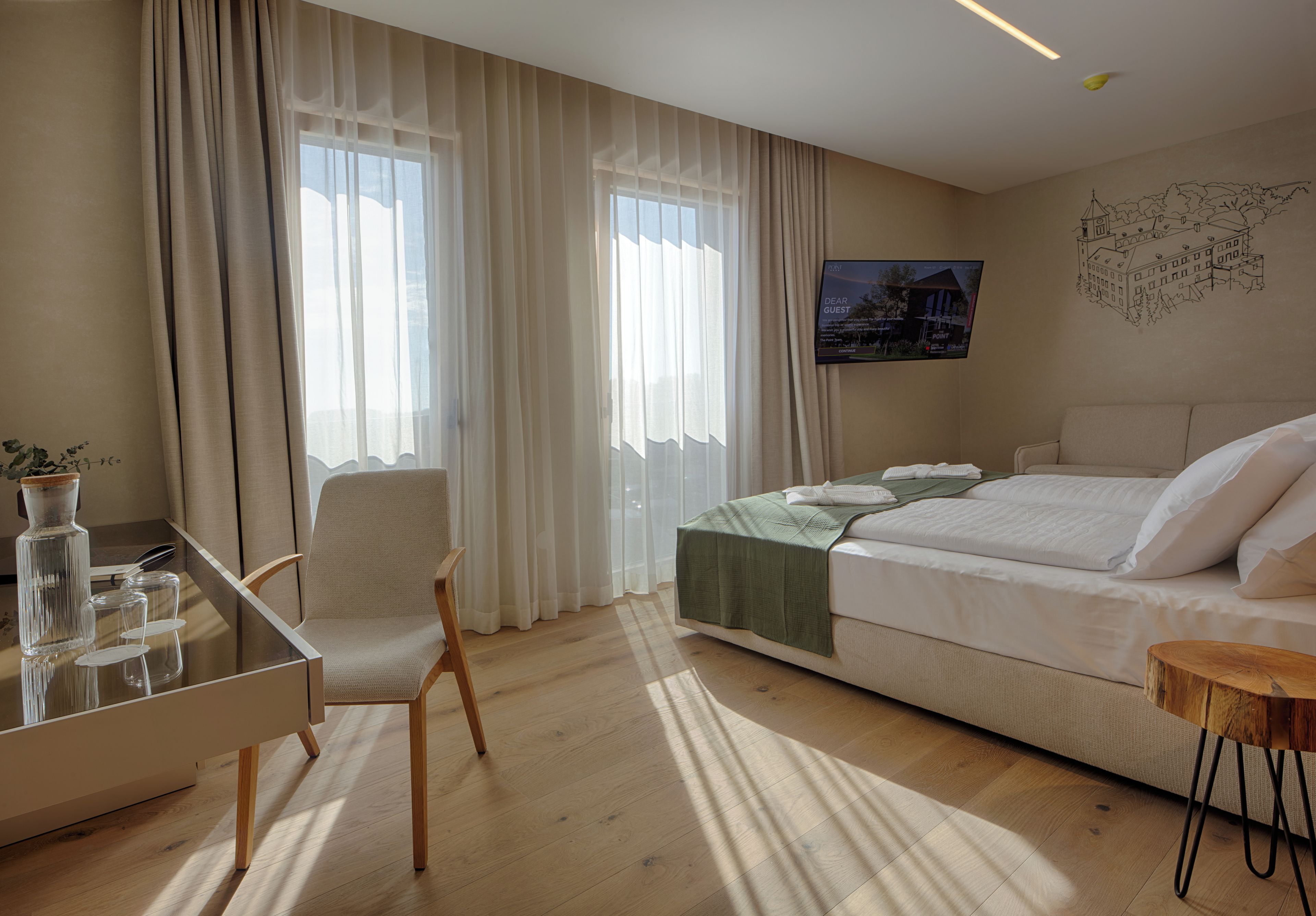 A hotel room with a bed, a desk, a chair, and a television on the wall.