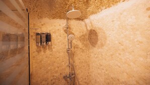Ducha con cabezal redondo, puerta de cristal y pared con diseño de panal.