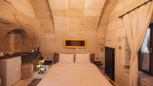 Una habitación con paredes de piedra, una cama, una pequeña kitchenette y una ventana con cortinas.