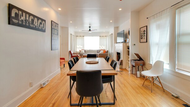 A spacious dining area with a long table, chairs, ceiling fans, and a view of a living room with a sofa and a fireplace. - Pool Table! Pet-Friendly Haven 6 Mi to Rate Field (Chicago)