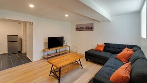 A modern living room with a sofa, a wooden coffee table, a television on a stand, and a cityscape painting on the wall. - Pool Table! Pet-Friendly Haven 6 Mi to Rate Field (Chicago)