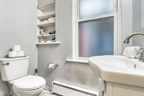 Un bagno con il water, un lavandino, una finestra e uno scaffale con articoli da toilette.