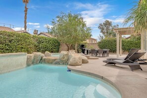 A pool with rocks, lounge chairs, and a pergola. - Desert Sanctuary | Pool, Spa & Sleeps 12 (Indio)