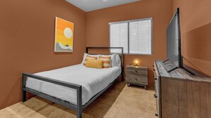 A bedroom with a bed, a nightstand, a dresser, a ceiling fan, a window with blinds, and a wall-mounted TV. - Desert Sanctuary | Pool, Spa & Sleeps 12 (Indio)