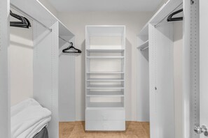 A walk-in closet with white shelving units, a hanging rod, and a folded white towel. - Desert Sanctuary | Pool, Spa & Sleeps 12 (Indio)