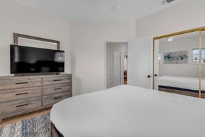 A bedroom with a bed, a TV on a wooden dresser, and a door leading to another room. - Desert Sanctuary | Pool, Spa & Sleeps 12 (Indio)
