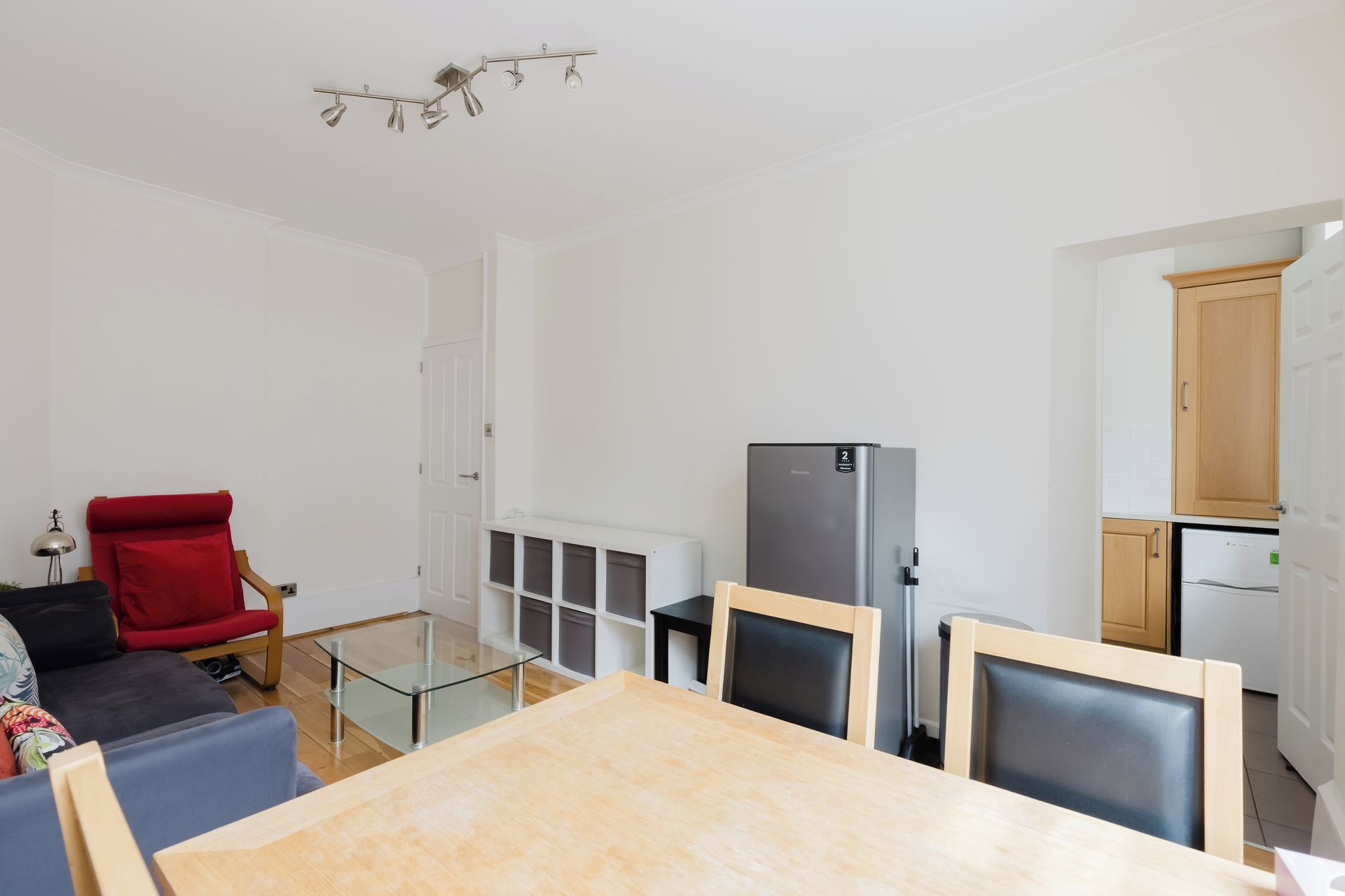 A modern living room with a glass coffee table, a red chair, a refrigerator, and a dining table.