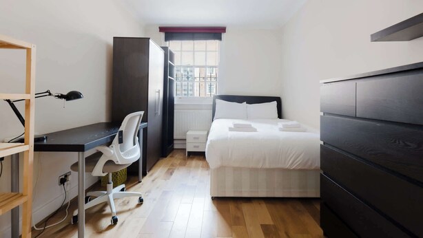 Een slaapkamer met een bed, bureau, stoel, kast en raam.