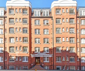 A multi-story brick building with a symmetrical facade, multiple windows with metal railings, and a central entrance with steps. - Spacious 2BD Flat by the British Museum (Greater London)