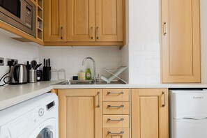 A kitchen with wooden cabinets, a stainless steel sink, a kettle, a coffee maker, and a white refrigerator. - Spacious 2BD Flat by the British Museum (Greater London)