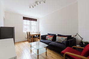 Ein modernes Wohnzimmer mit einem Glastisch, einem dunklen Sofa und einem Essbereich mit einem Holztisch und Stühlen.