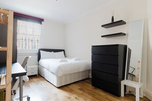A bedroom with a bed, a desk, a dresser, and a window with a view of buildings. - Spacious 2BD Flat by the British Museum (Greater London)