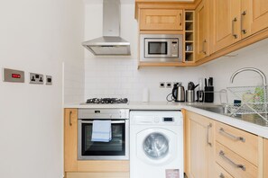 A compact kitchen with a gas stove, microwave, oven, and washing machine. - Spacious 2BD Flat by the British Museum (Greater London)