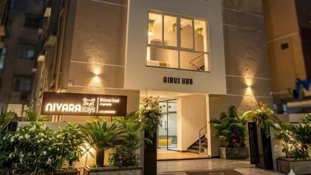 Ein mehrstöckiges Hotel mit modernem Design, das eine markante Eingangspforte mit einer Treppe und ein Schild mit der Aufschrift AIRUS HUB zeigt.
