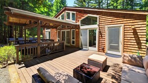 Eine Holzterrasse mit Gartenmöbeln, einem überdachten Sitzbereich und einer großen Schiebetür.