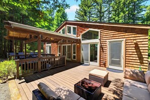 Eine Holzterrasse mit Gartenmöbeln, einem überdachten Sitzbereich und einer großen Schiebetür.