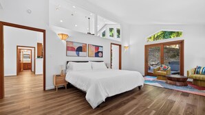 Ein modernes Schlafzimmer mit einem großen Bett, einer Couch und einem Esstisch. Zwei Fenster und eine Tür zu einem anderen Raum.