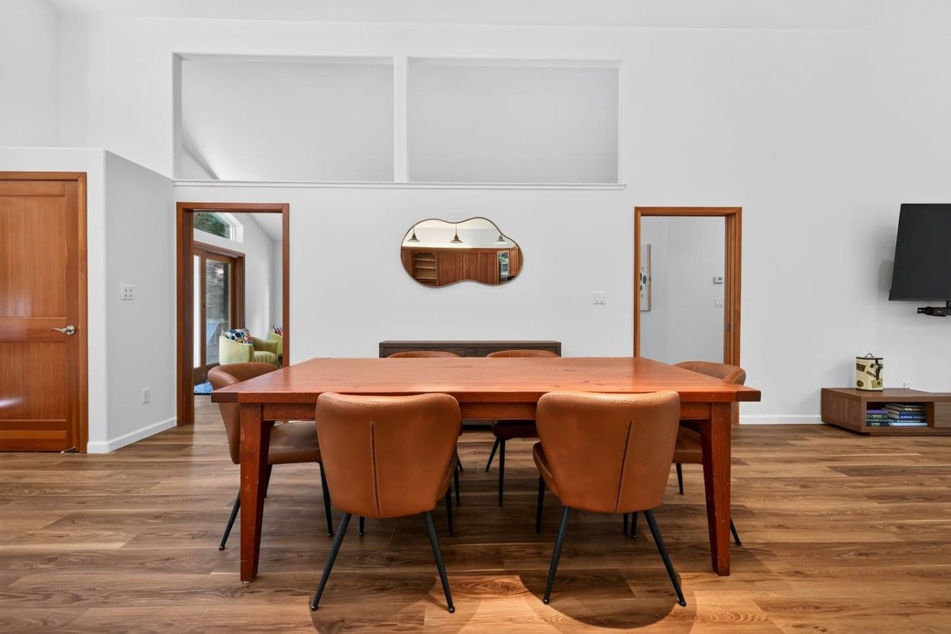 Un comedor con mesa de madera y cuatro sillas, una lámpara fijada en la pared y un televisor colgado.