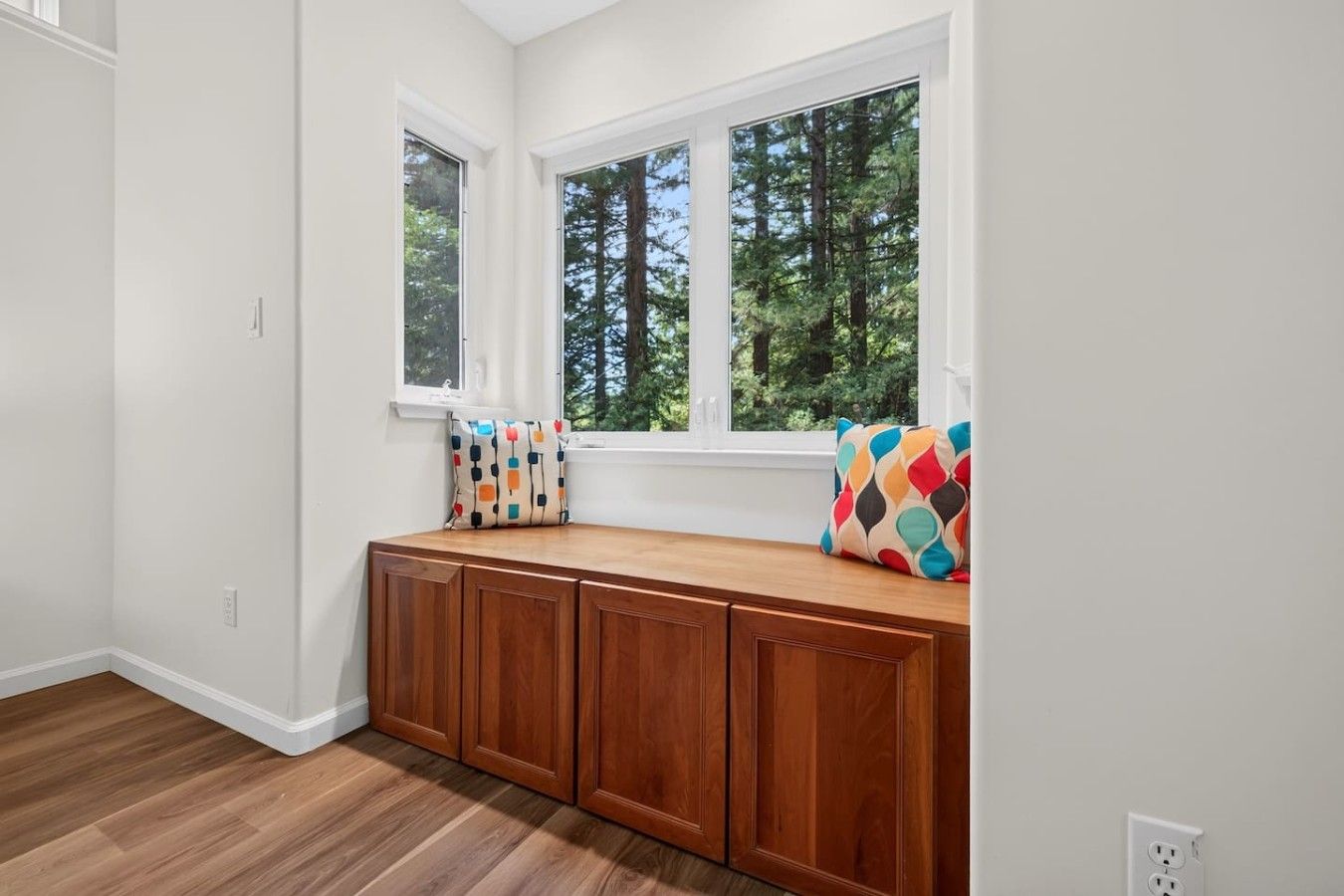 A room with a built-in bench against a wall with large windows overlooking a forest.