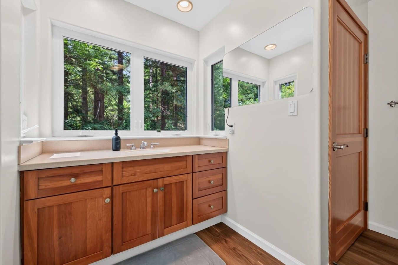A modern bathroom with a wooden vanity, a sink, and a window with a view of trees.