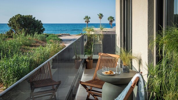 Ein Balkon mit Meerblick, Holzstühle, ein Tisch mit Essen und Kübelpflanzen.