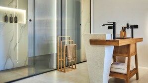 Ein modernes Badezimmer mit Marmor-Waschtisch, einer Duschkabine aus Glas und einem hölzernen Handtuchhalter.