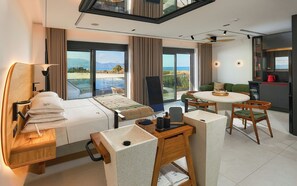 A modern hotel room with a bed, a dining area, a kitchen, and large windows offering a view of the sea. - Diastar Luxury Suite in Heraklion Crete A3 (Xeropotamos)