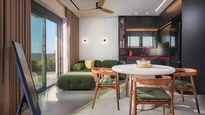 Ein modernes Wohnzimmer mit einer Couch, einem Esstisch und Stühlen. Es gibt eine Küchenzeile mit Kühlschrank und Spüle.