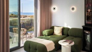 Ein modernes Schlafzimmer mit einem grünen Schlafsofa, einem kleinen runden Tisch und Meerblick durch große Fenster.